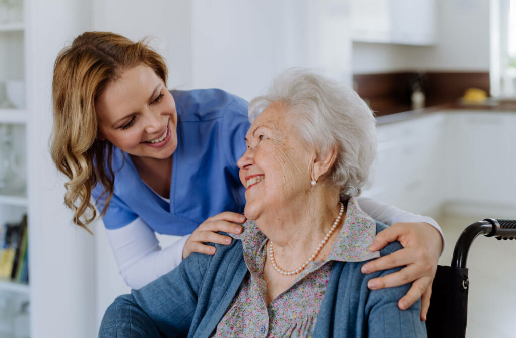 An older adult woman in a wheelchair, smiling and talking to a caregiver